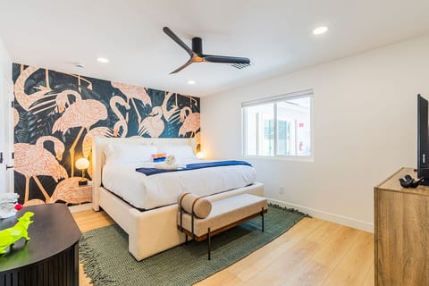 Inviting bedroom w/ statement mural, plush bedding, & ceiling fan for a cozy night’s sleep.