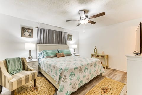 The spacious master suite offers a king bed dressed in soft coral linens, a cozy reading chair, and a flat-screen TV. A calm, coastal escape with room to spread out — perfect for parents to recharge after a full day of family fun.