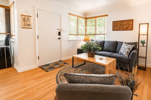 The main living room from another angle: a comfy sofa, oak floors, and big bright windows. Room to spread out.