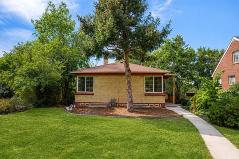 A 1940s yellow-brick bungalow on a quiet residential street, with a covered front porch and a green front lawn.