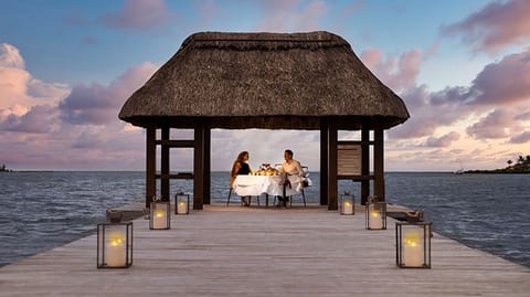 A romantic dinner setup surrounded by lanterns and overlooking the calm sea