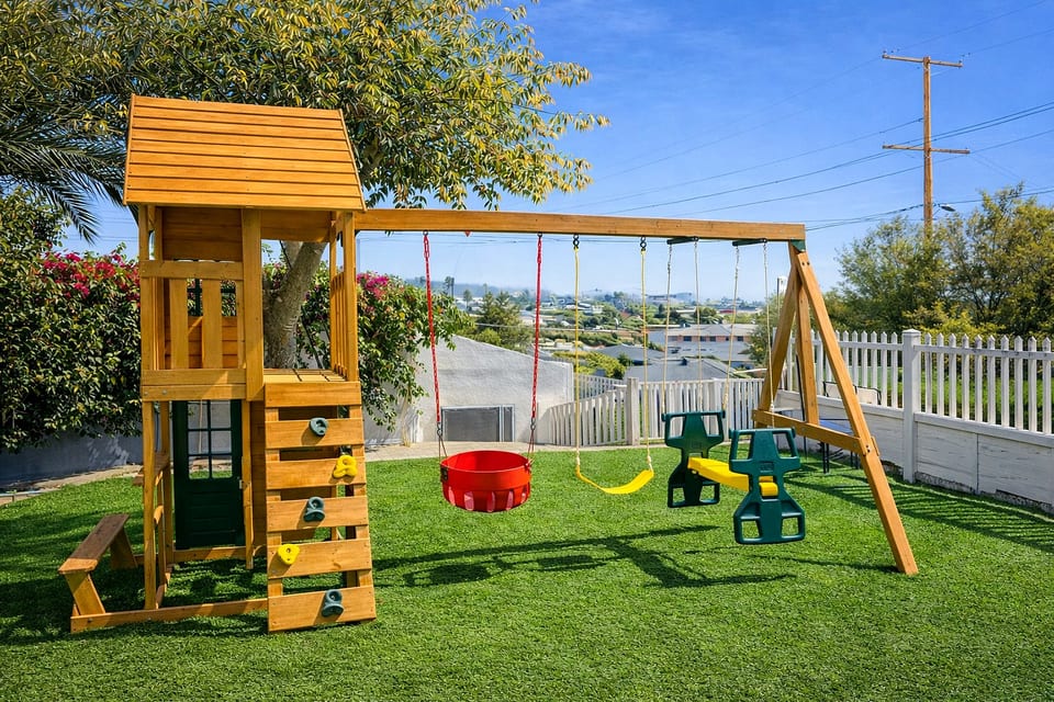 Fenced yard with playset, swings, and turf—family‑friendly fun