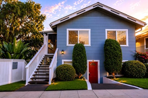 Charming blue bungalow with red door, manicured garden, evening glow