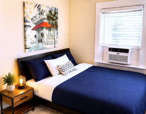 Bright queen bedroom with AC, plush bedding, and stylish decor