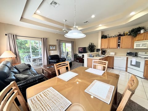 Bright and spacious open-concept living area featuring vaulted tray ceilings, a fully equipped kitchen, comfortable seating, and sliding glass doors leading out to a private screened balcony.