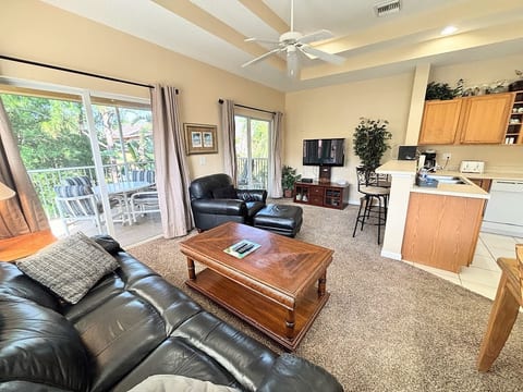 Comfortable living area with leather seating, large TV, breakfast bar seating, and sliding glass doors leading to the screened balcony.