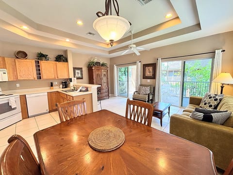 Bright and spacious open-concept living area featuring vaulted tray ceilings, a fully equipped kitchen, comfortable seating, and sliding glass doors leading out to a private screened balcony.