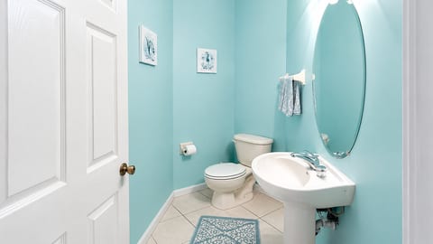 Convenient half bathroom with pedestal sink, tile flooring, and bright coastal-colored walls.