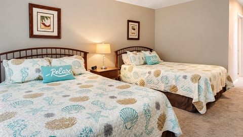 Bright bedroom with two comfortable beds, warm bedside lighting, and a relaxed beachy feel.