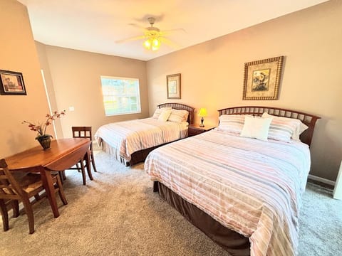 Spacious bedroom featuring two beds, ceiling fan, small dining/work table, and plenty of natural light.