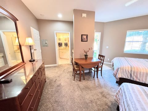 Comfortable bedroom layout with two beds, dresser storage, small dining/work area, and easy access to the bathroom.