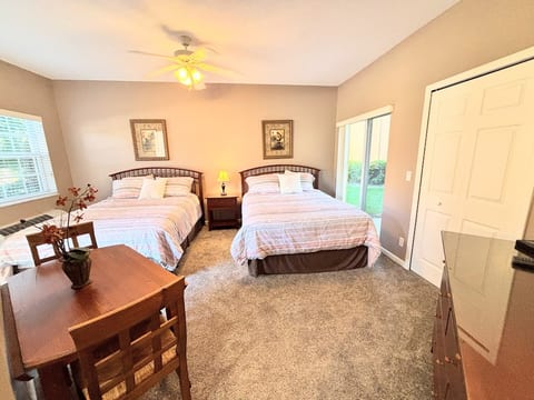 Bright bedroom featuring two beds, ceiling fan, dresser storage, and a cozy table with seating.