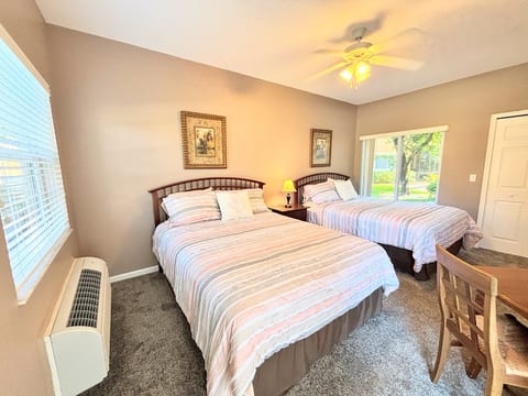 Spacious bedroom with two beds, ceiling fan, dresser storage, and a bright window view.