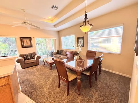 Open dining and living area with comfortable seating, tray ceilings, large windows, and sliding glass doors leading to the private balcony.