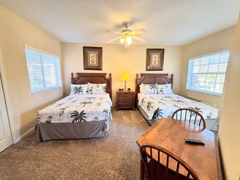 Spacious bedroom featuring two comfortable beds, ceiling fan, small dining/work table, and plenty of natural light.