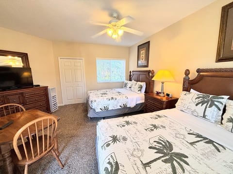 Spacious bedroom with two beds, dresser storage, TV, and a small table with seating.