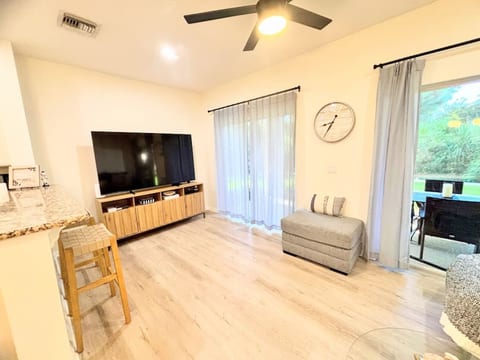 Modern living area with wood-look flooring, large TV, stylish decor, and sliding glass doors that open to the outdoor patio space.