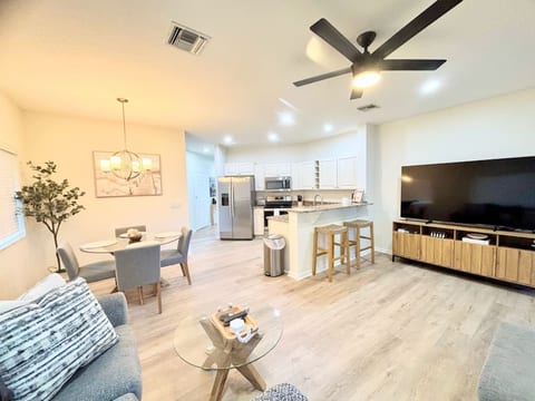 Spacious modern open-concept living area with stylish furnishings, large TV, dining space, updated kitchen, and bright wood-look flooring throughout.