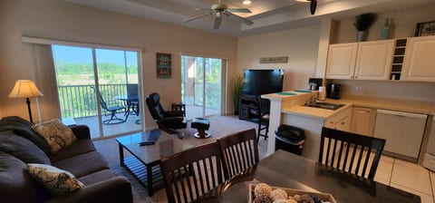 Open-concept living, dining, and kitchen area with high ceilings, comfortable seating, and access to the private screened balcony.