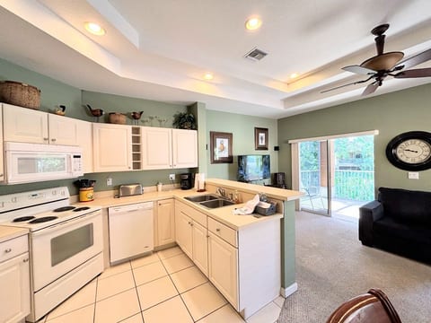 Open-concept kitchen and living area with high ceilings, bright natural light, and sliding glass doors leading to the balcony.