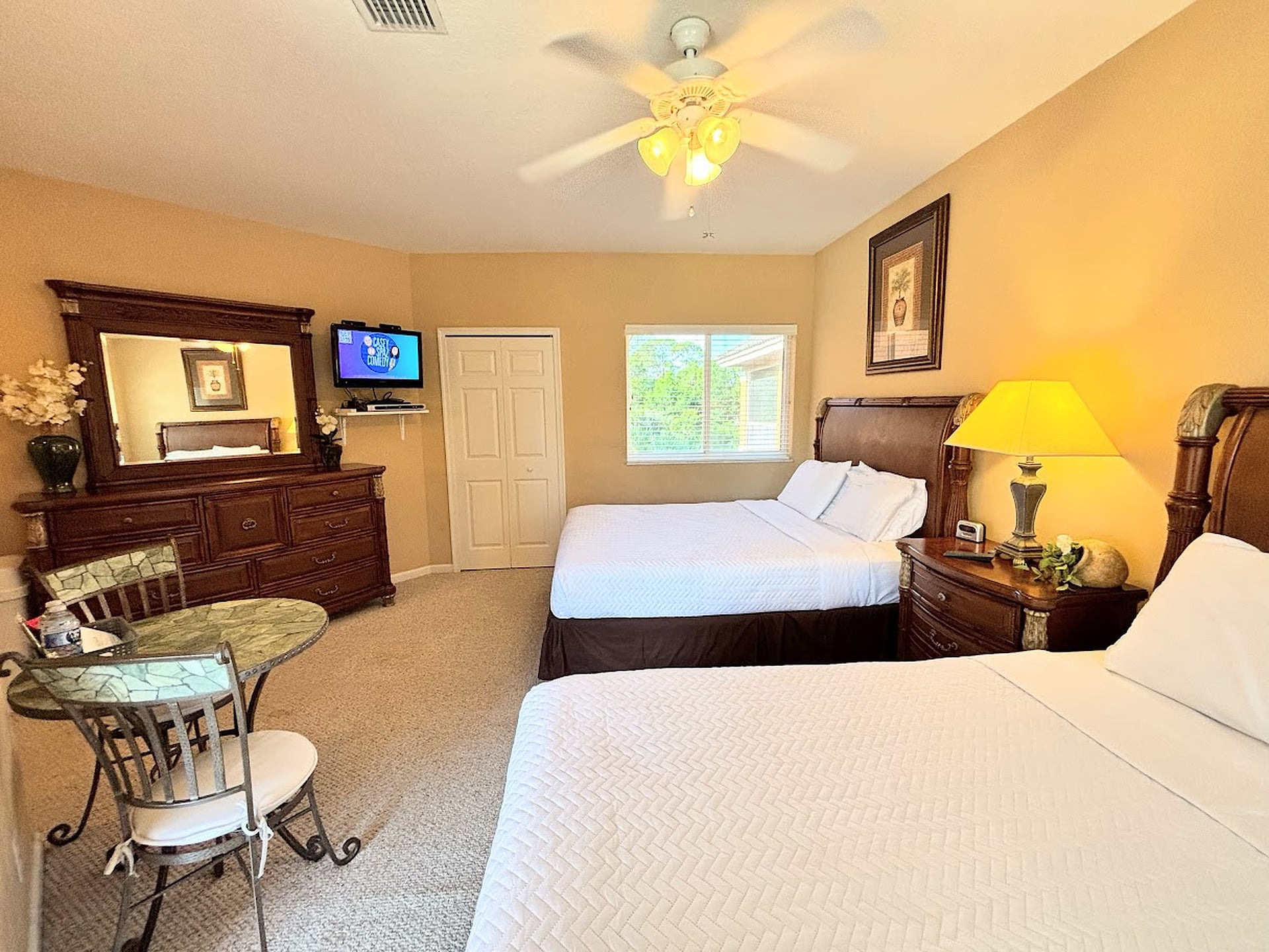 Spacious bedroom featuring two comfortable beds, dresser storage, TV, and a small table with seating.