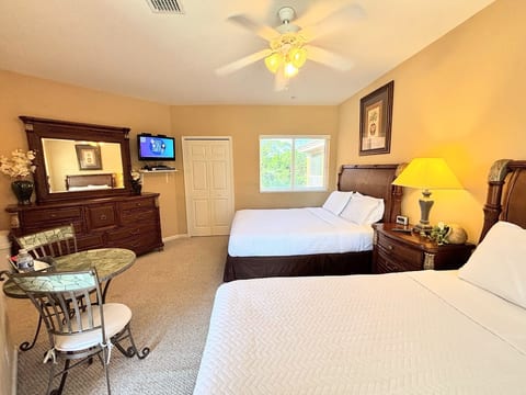 Spacious bedroom featuring two comfortable beds, dresser storage, TV, and a small table with seating.