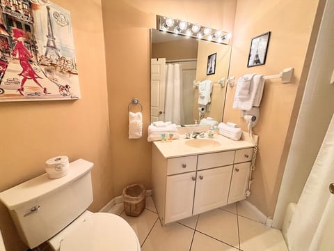 Clean bathroom with vanity storage, toilet, tile flooring, and bright mirror lighting.