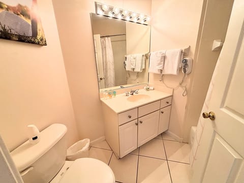 Clean bathroom with vanity storage, toilet, tile flooring, and bright mirror lighting.