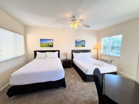 Comfortable bedroom featuring two beds, ceiling fan, dresser storage, and plenty of natural light.