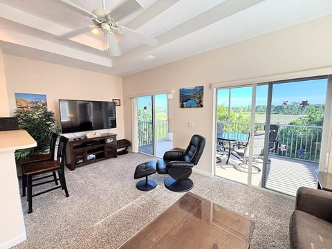 Spacious living area with large TV, cozy seating, and sliding glass doors leading to the screened balcony with peaceful views.
