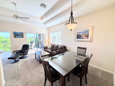 Bright dining and living area with high ceilings, comfortable seating, large windows, and access to the private screened balcony.