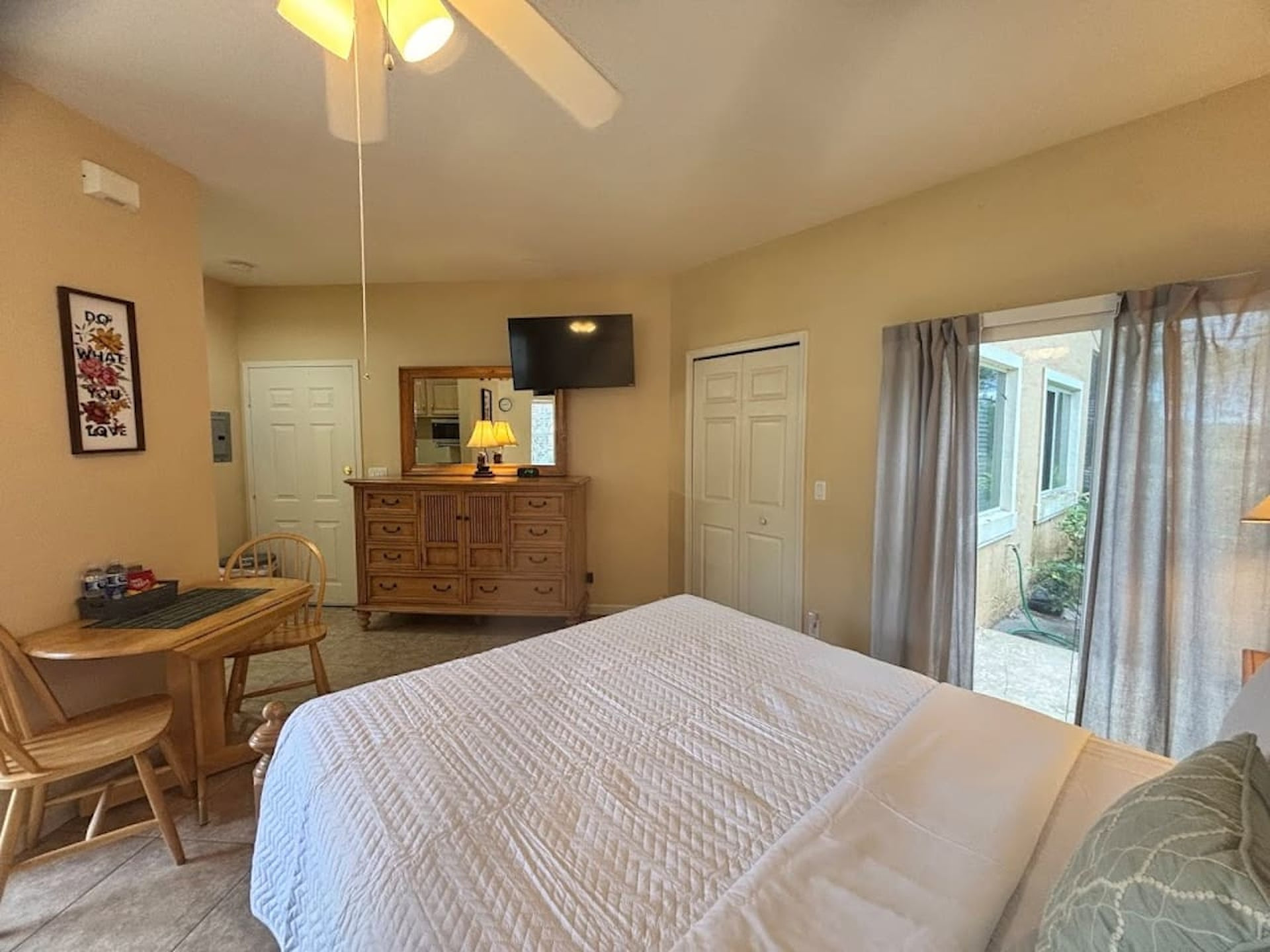 Spacious bedroom featuring a large bed, dresser storage, TV, small table with seating, and plenty of natural light.