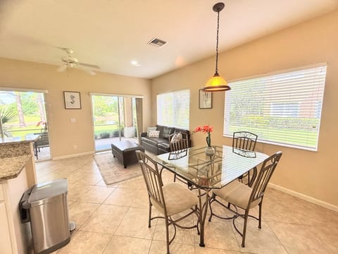 Bright open dining, kitchen, and living area with tile flooring, comfortable seating, and access to the screened patio.