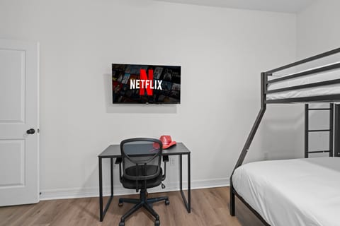 Bright bedroom with bunk bed, workspace, and wall-mounted TV