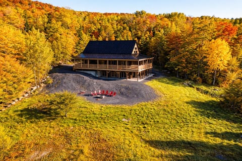 Large cabin surrounded by vibrant fall foliage with a wraparound deck, fire pit, and scenic mountain views.