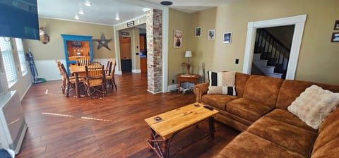 Spacious open-concept living and dining area featuring rustic wood furnishings, hardwood floors, comfortable sectional seating, and plenty of natural light.