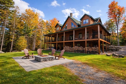 Large log cabin with a wraparound porch, outdoor fire pit, and spacious yard surrounded by beautiful trees and seasonal views.