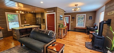 Open-concept living area with a full kitchen, wood stove, workspace, and rustic wood finishes throughout.