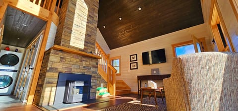 Living room with a stone fireplace, vaulted ceilings, TV, and loft access.