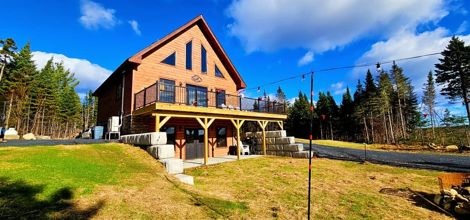 Modern log cabin with a spacious deck, outdoor seating, and scenic forest views.