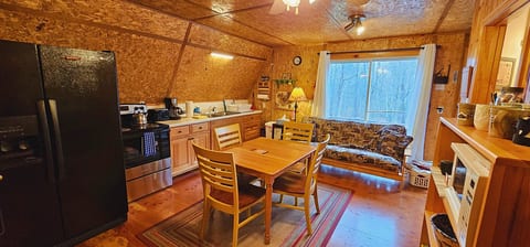 Rustic cabin kitchenette and dining area with full-size appliances, a cozy futon, and peaceful woodland views through the large picture window.