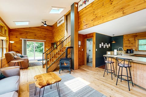 Open-concept cabin interior with a cozy wood stove, vaulted ceilings, and a fully equipped kitchen for relaxing mountain getaways.