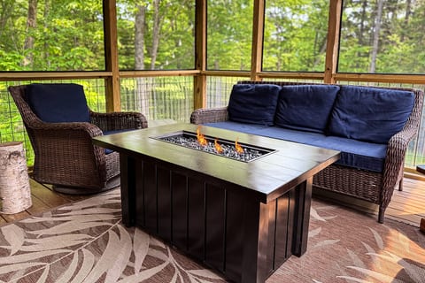 Screened-in porch with comfortable seating, a cozy fire table, and peaceful forest views for year-round relaxation.