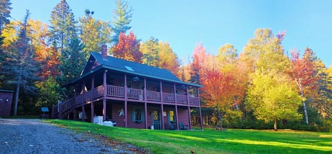 Spacious log cabin surrounded by colorful fall foliage, featuring a wraparound porch and peaceful wooded setting.