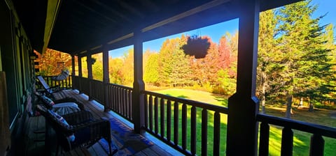 Covered wraparound porch with comfortable seating and stunning fall foliage views, perfect for relaxing in a peaceful woodland setting.