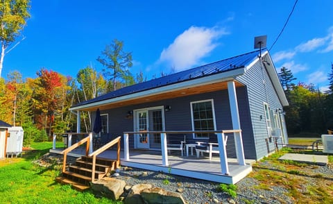 Modern lakeside cottage with a covered porch, peaceful surroundings, and comfortable outdoor seating for relaxing getaways.