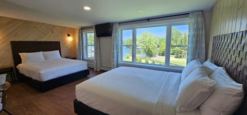 Cozy queen bedroom with large windows, natural wood accents, and peaceful views of the property grounds.