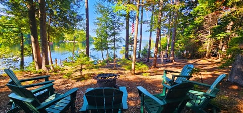 Peaceful lakeside fire pit with Adirondack chairs, towering pines, and beautiful water views for relaxing evenings by the lake.