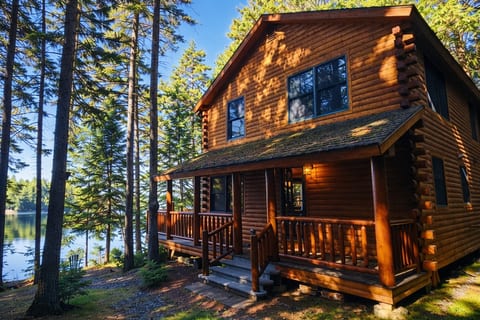 Stunning waterfront log cabin surrounded by towering pines, featuring a covered porch and peaceful lakefront views for the ultimate getaway.