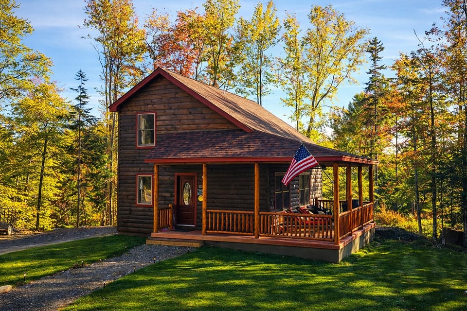 Beautiful log cabin retreat with a wraparound porch, spacious lawn, and vibrant fall colors creating the perfect woodland getaway.
